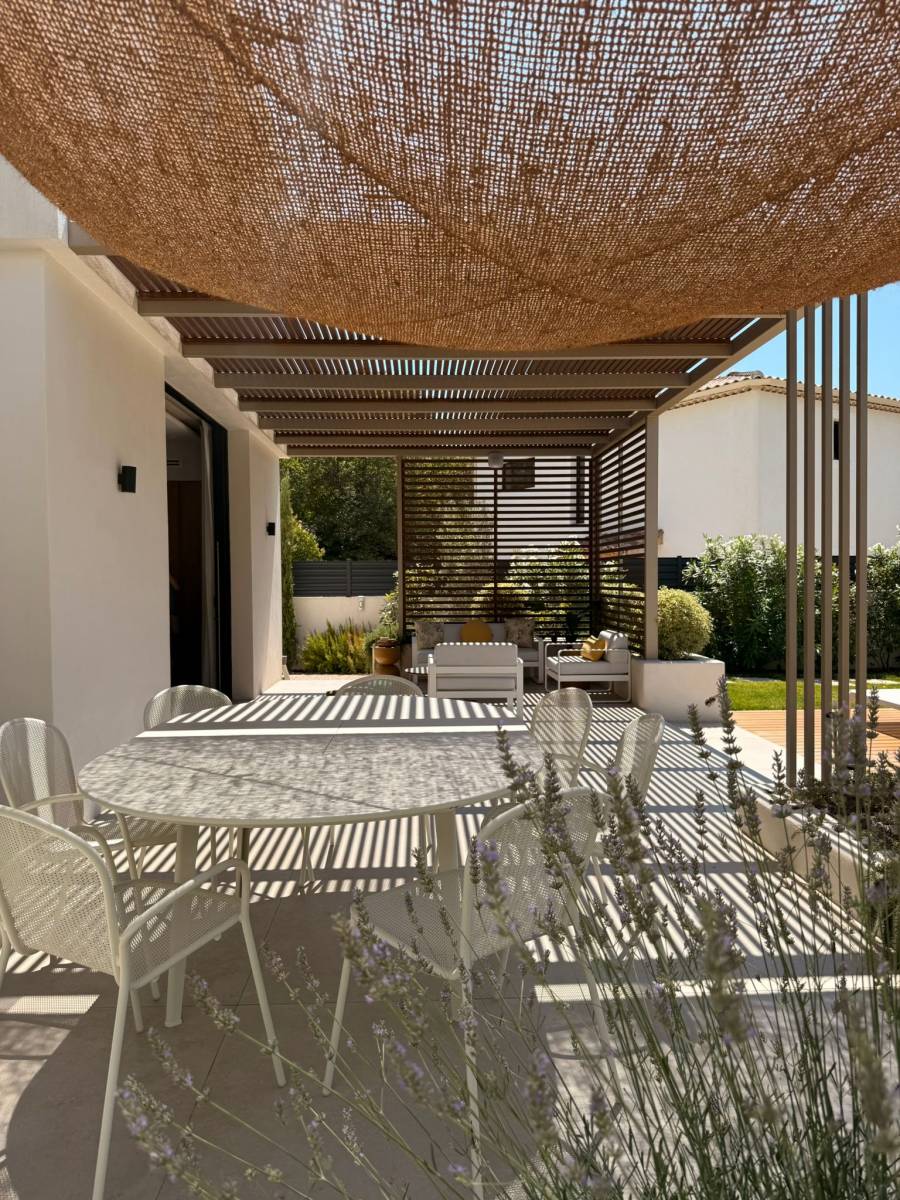 Vue en perspective de la pergola avec brise-soleil latéraux — un coin repas extérieur parfaitement intégré à l’environnement.